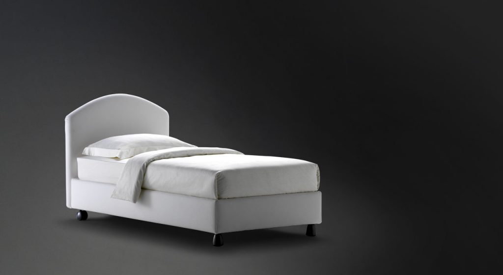 Magnolia Single bed. Padded headboard and base with white fabric and black legs on a black background.