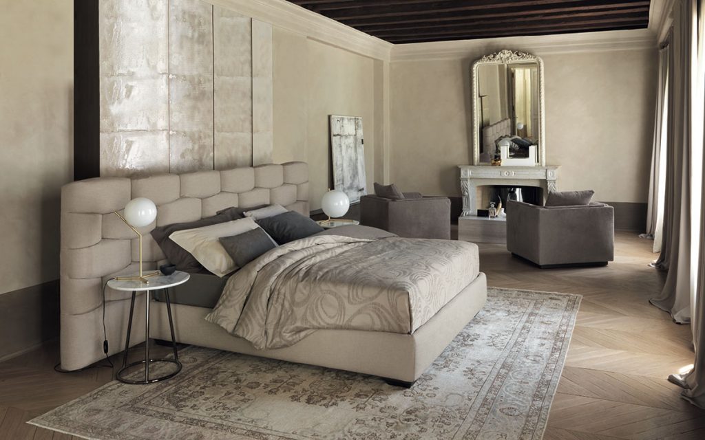 Beige Majal wide bed with geometric shapes on the headboard, mattress and bedding in a bedroom.