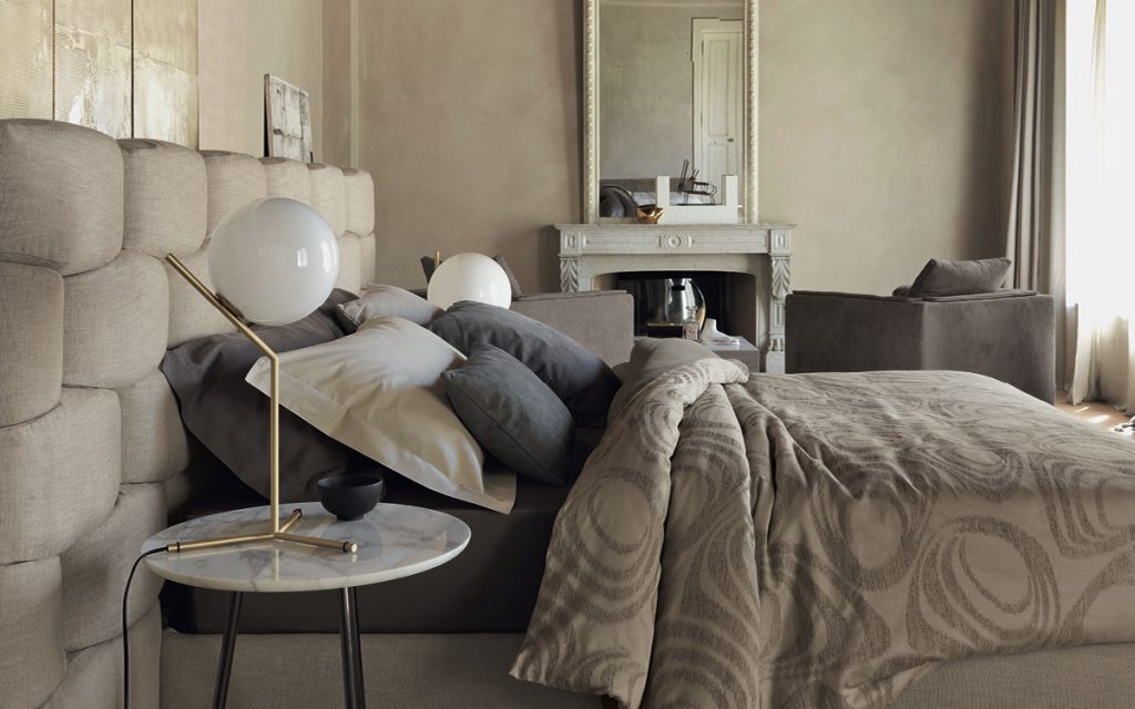 Beige Majal wide bed with geometric shapes on the headboard, mattress and bedding in a bedroom.