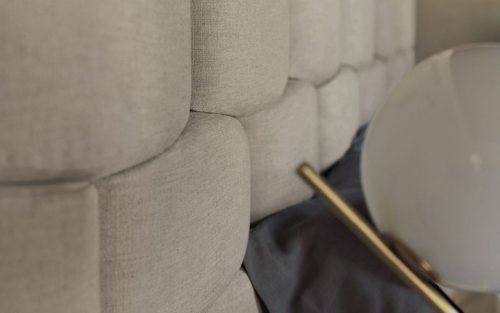 Closeup of beige Majal wide bed with geometric shapes on the headboard, mattress and bedding in a bedroom.