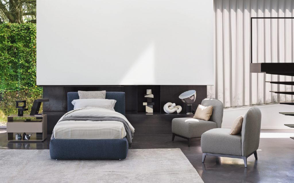 Merkurio Single bed. Base and headboard upholstered in blue fabric with four legs in a bedroom.