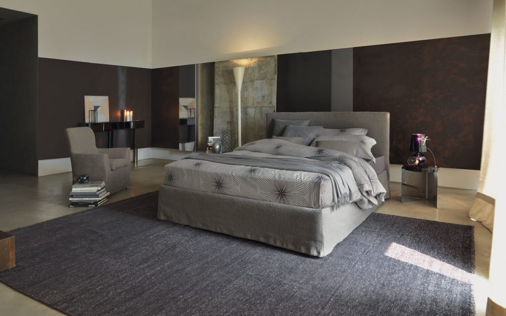 Notturno Shabby Chic Bed. Base and backrest covered in gray fabric with bedding in a bedroom.