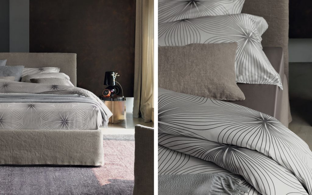 Closeup of Notturno Shabby Chic Bed. Base and backrest covered in gray fabric with bedding in a bedroom.