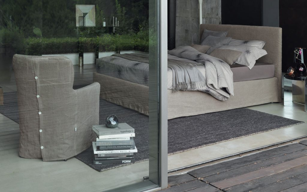 Notturno Shabby Chic Bed. Base and backrest covered in gray fabric with bedding in a bedroom.