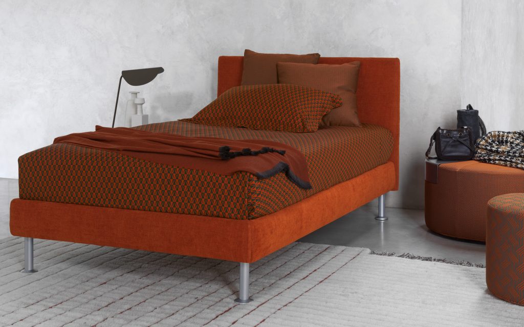 Notturno Single bed. Base and backrest covered in red fabric and legs with bedding in a bedroom.