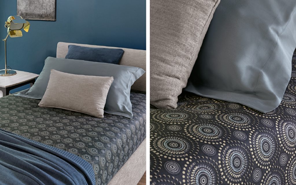 Closeup of Notturno Single bed. Base and backrest covered in gray fabric and legs with bedding in a bedroom.