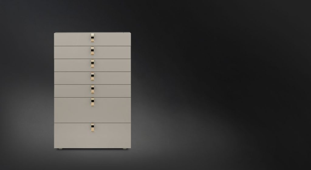 Tallboy Splendor. White structure with seven drawers with seven golden handles on a black background.