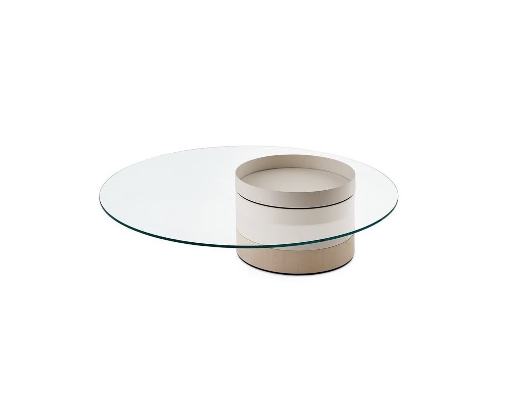 A **Haumea Coffee Table** featuring a round transparent glass top supported by a cylindrical beige base, combining modern elegance with minimalist design