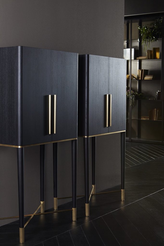 Tama: Two brown wooden storage drawers with gold handles and four legs against a gray wall.
