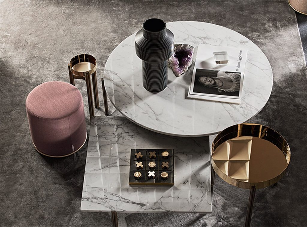 Four Twelve coffee tables. Two golden round tops and two in marble, one in round and one in square shape with three bronze legs in a living room.