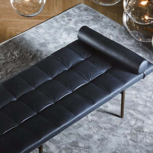Rectangular Twelve Daybed upholstered in black leather with rectangular pattern and four gold legs on a gray background.