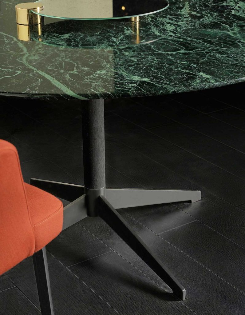 Closeup of Zen Black table, round top in green and black marble and central black leg in a dining room.