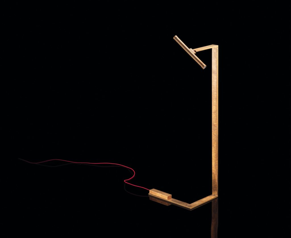 Let Flat Lamps with brass pipe structure, multi directional light, power lead with red silk cover, counterweight in stone on a black background.