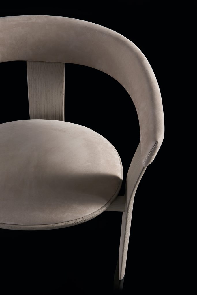 Closeup of beige Noce Chair, structure and three legs in wood. Padded seat and backrest with leather on a black background.