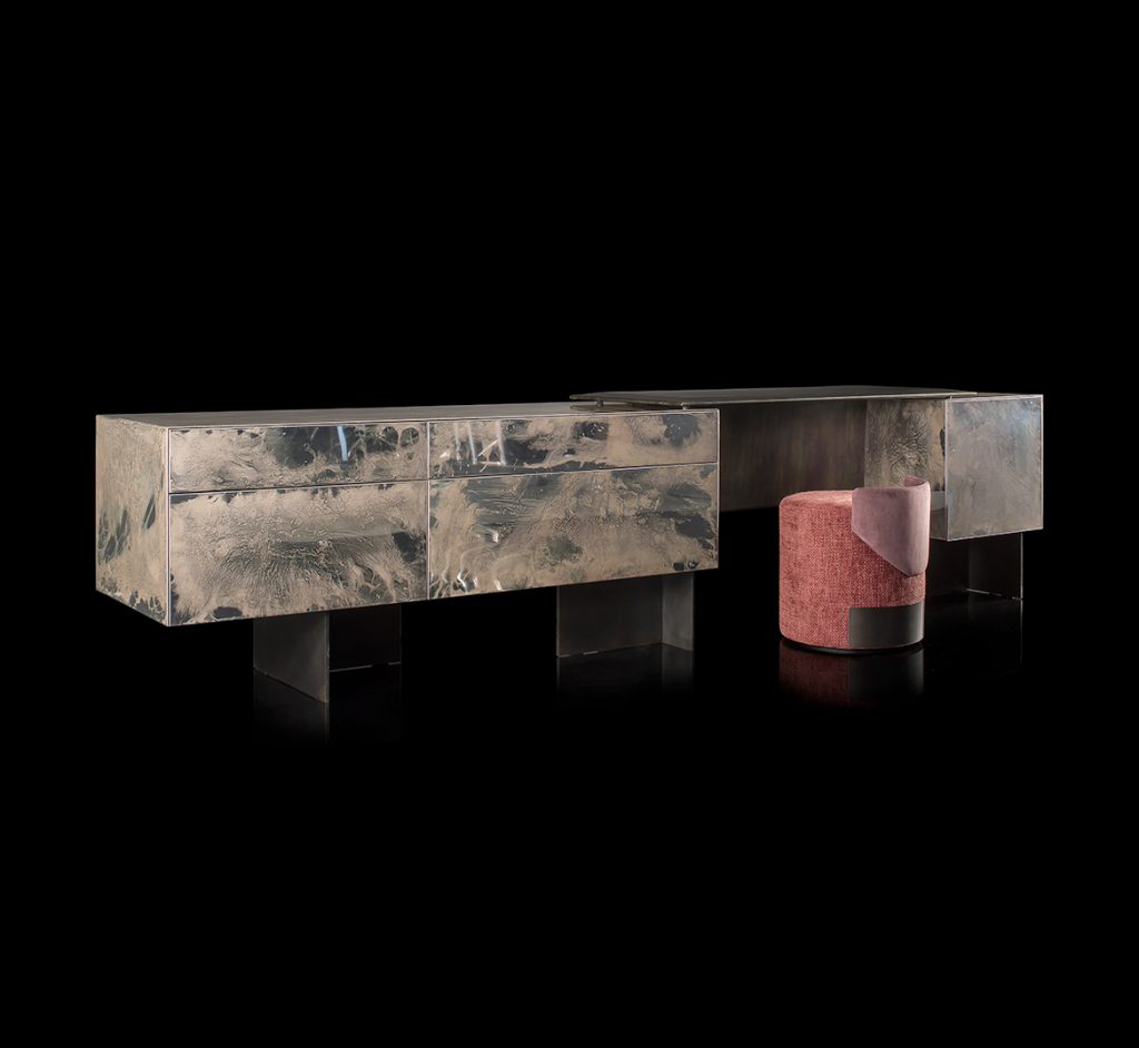 Noctis Vanity cabinet with three doors. Outside covered with burnished steel, three legs in black steel and a stool on a black background.