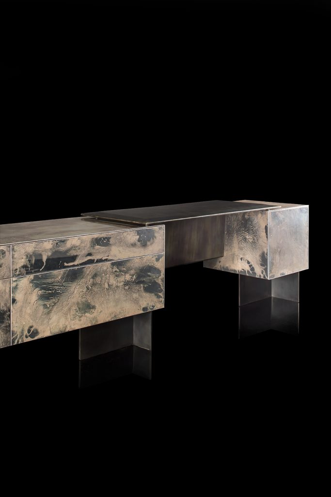 Closeup of Noctis Vanity cabinet with three doors. Outside covered with burnished steel, three legs in black steel on a black background.