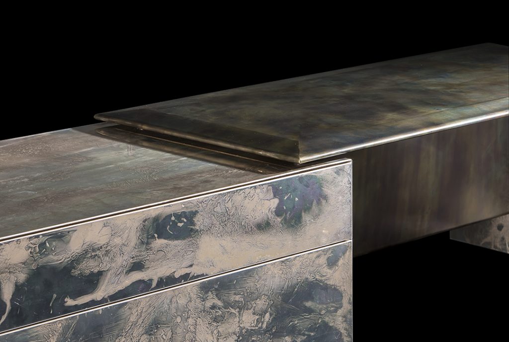 Closeup of Noctis Vanity cabinet with three doors. Outside covered with burnished steel, three legs in black steel on a black background.