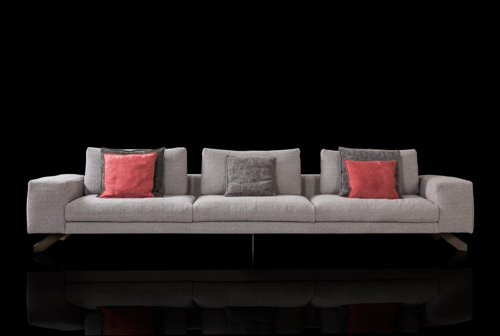 Opus Sofa upholstered in gray fabric with four legs in black steel with poufs and a table on a black background.
