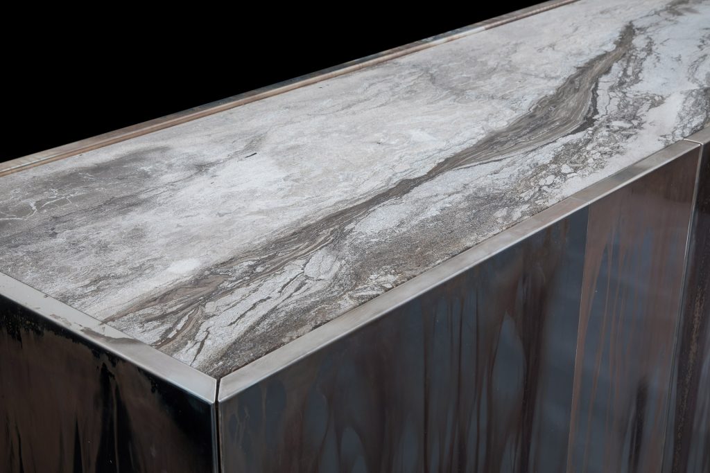 Side X Evo table, structure in natural wood covered with silver metal and top in brown and white marble pattern stone on a black background.