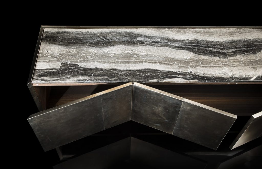 Side X Evo table with three doors, structure in natural wood covered with silver metal and top in brown and white marble pattern stone on a black background.