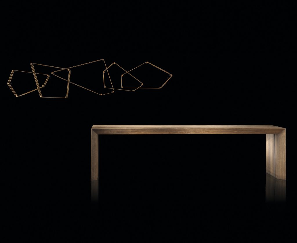 Tangram bookcase made of irregular polygons joined together. Structure in natural burnished brass attached to a black wall on a black background.