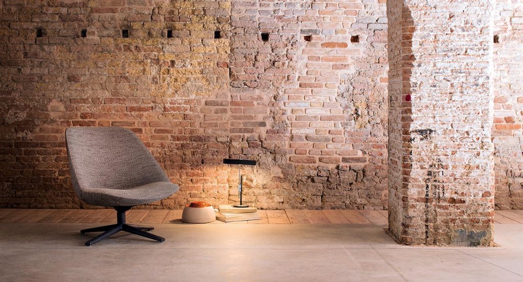 Swiveling and tilting Adele Armchair, gray upholstery cover and black wooden base with four spokes in a living room.