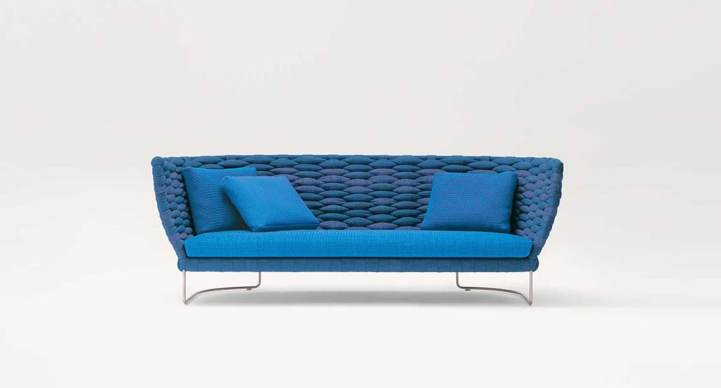 Ami Indoor Sofa: Blue upholstered sofa with woven sides and curved backrest with two silver legs on a white background.