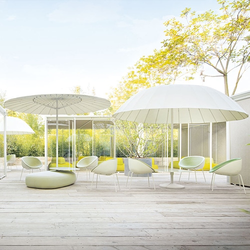 A serene outdoor setting featuring the Bistro Umbrella, shading a contemporary patio with lush greenery in the background
