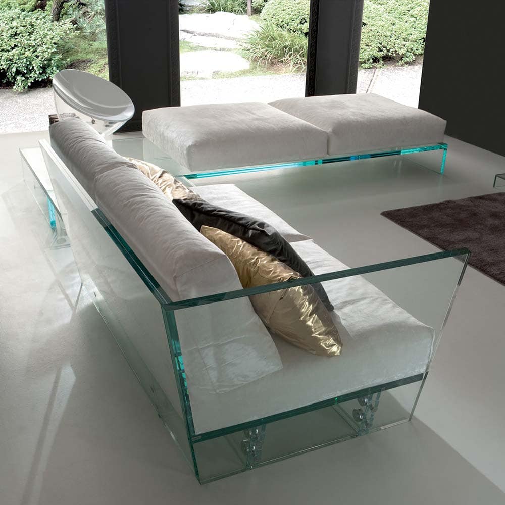 A contemporary sectional sofa with a transparent glass base, white cushions, and a sleek modern design, set in a bright living space with large windows