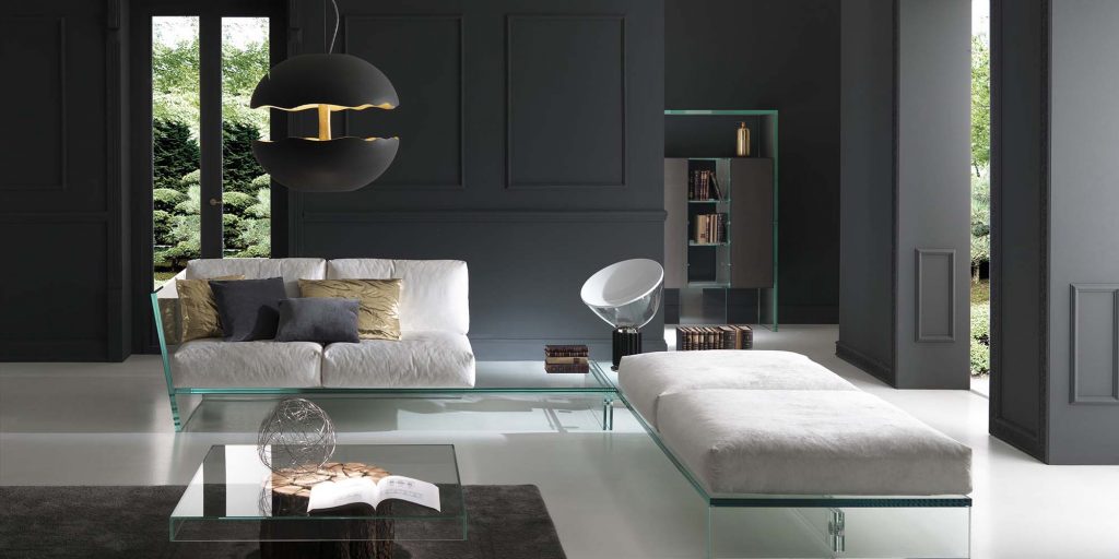 A modern living room featuring a sleek white sofa with a glass base, complemented by a matching chaise lounge, black accent walls, and contemporary lighting