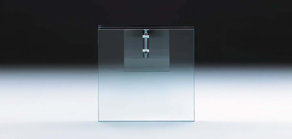 A sleek glass side table with a transparent, minimalist design. The structure features a floating metal fastener, adding a contemporary and sophisticated touch