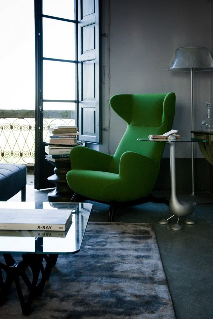 Ardea armchair with a green fabric upholstery and black wooden legs in a living room.