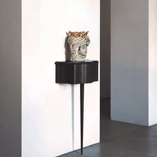 Carlino side table in brown color. Top with drawer and central leg against a white wall.