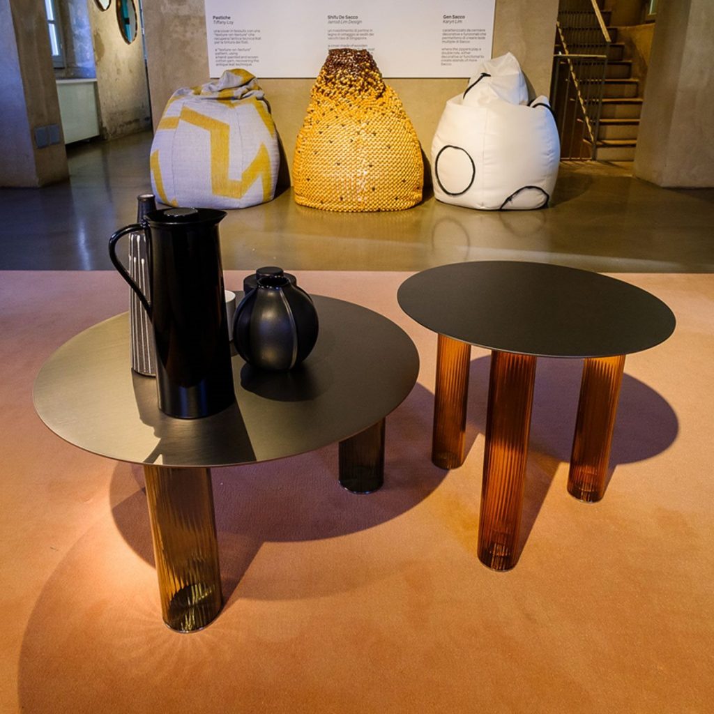 Two Echino coffee table. Round gray top and three semi transparent cilindrical legs in bronze in a living room.