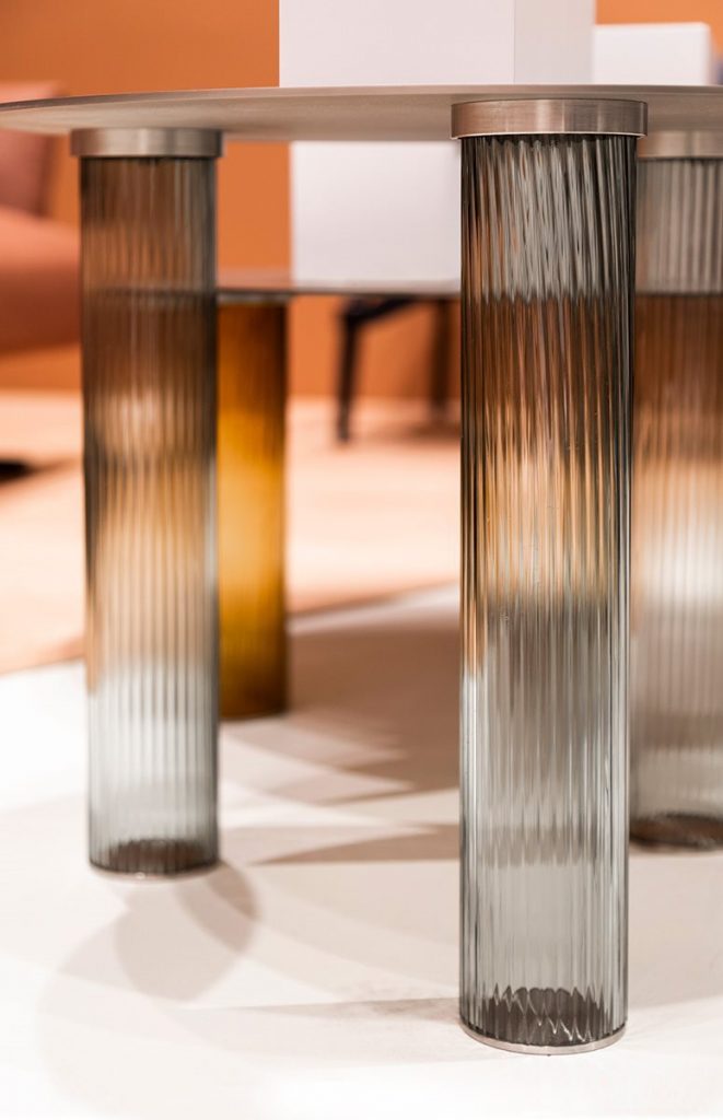 Closeup of Echino coffee table. Round black top and three semi transparent cilindrical legs in gray.