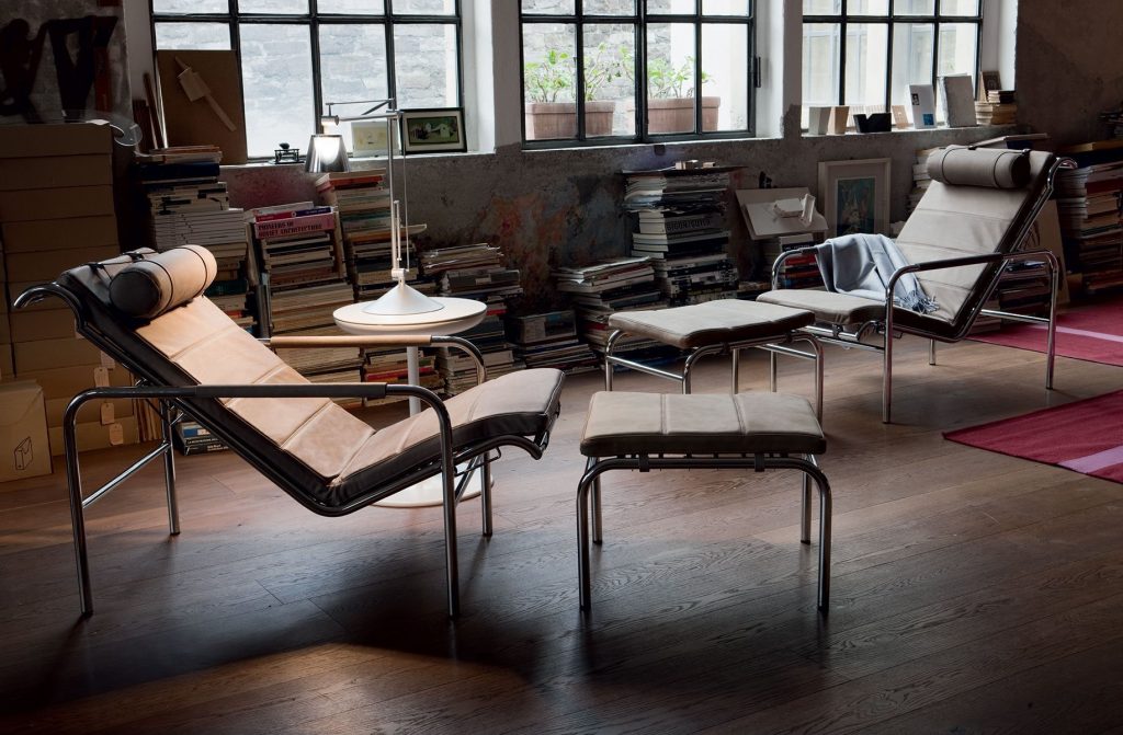 Two Genni lounge chairs with a contemporary design, featuring a wide, brown cushioned seat, a metal frame and stool in a living room.