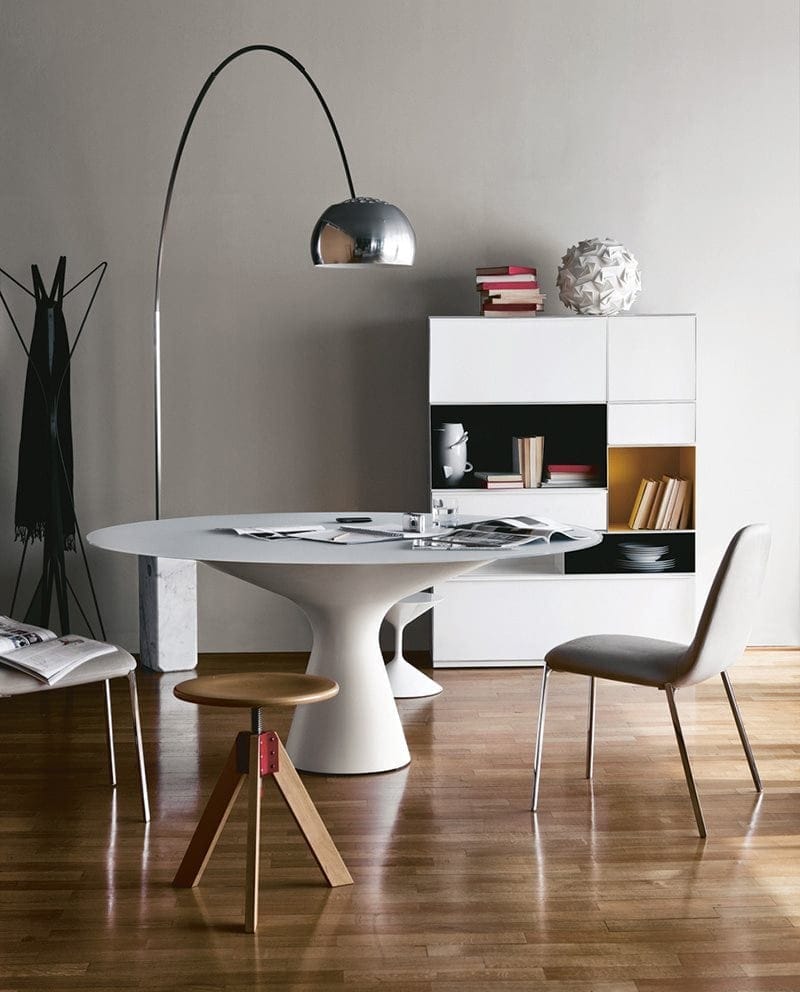 Giotto stool, round top and three legs in natural wood color next to a table.