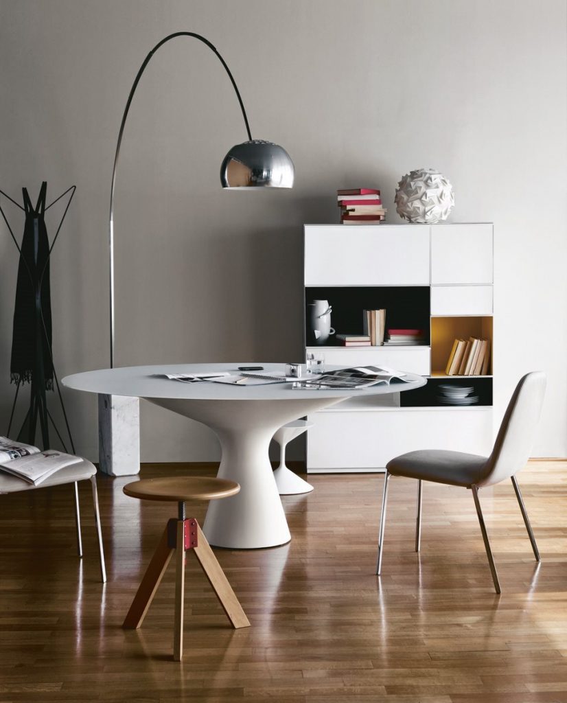 Giotto stool, round top and three legs in natural wood color next to a table.