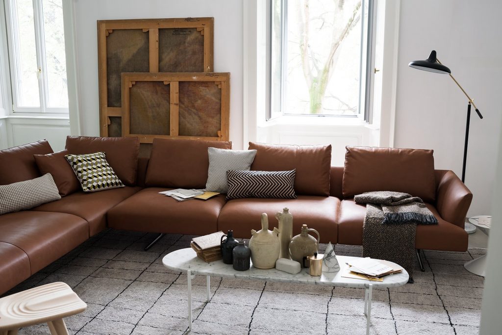 L shaped Hiro sifa with backrest and armrest in brown fabric and four black legs in a living room.