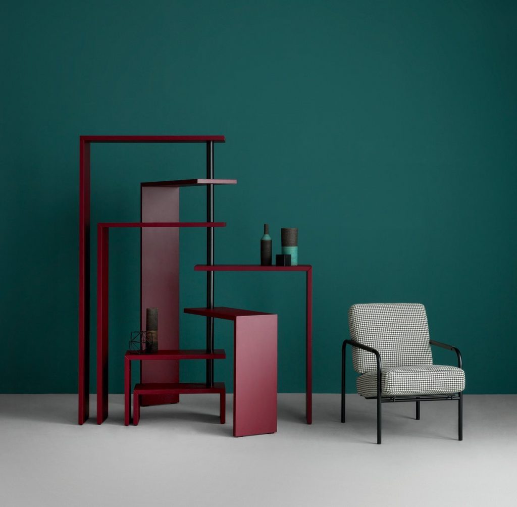 Red Joy bookcase with seven moveable shelves around a central tube on a white floor and green wall.