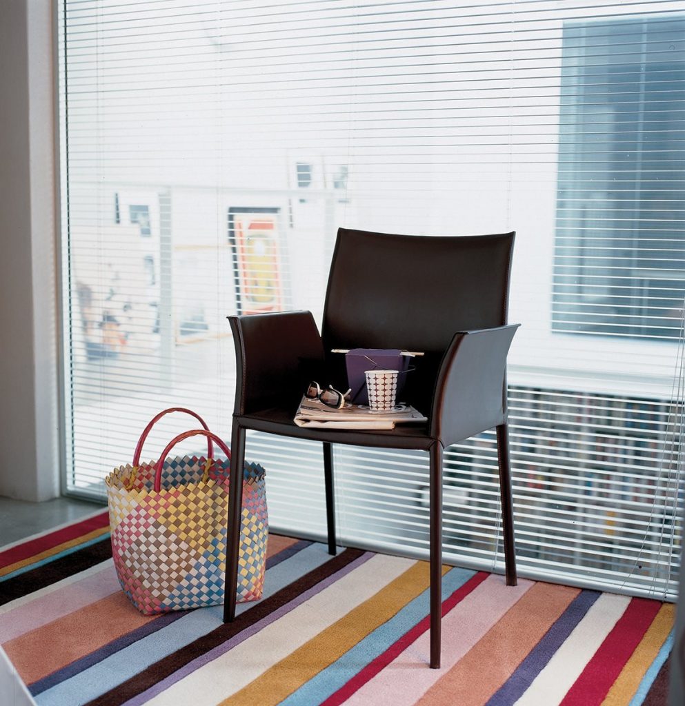 Lea chair featuring a high backrest and a upholstered seat, armrest and backrest in black fabric with four black legs in a office room.