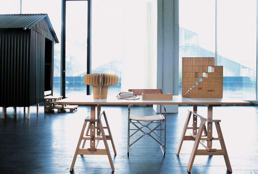 Square Leonardo table featuring a white wooden top and four wooden sturdy legs in a office.