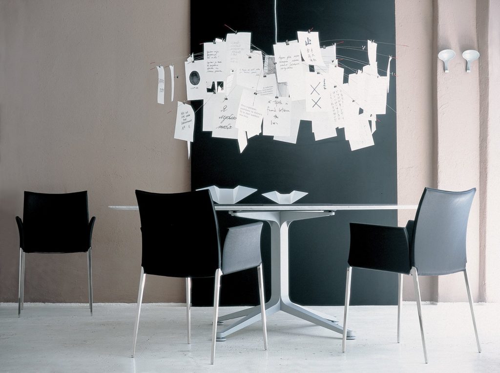 Three Lia chairs featuring a silver metal frame and four legs. Black cushioned seat, armrest and backrest in a dining room.