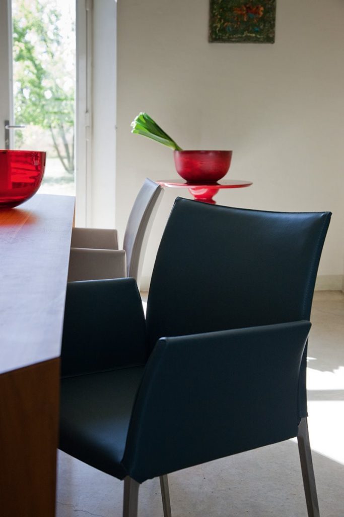 Two Lia chairs featuring a black metal frame and four legs. Cushioned seat, armrest and backrest one in black and one in beige in a dining room.