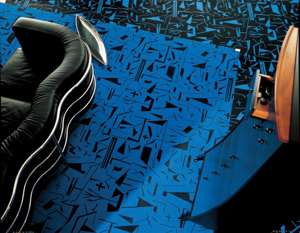Onda sofa featuring a curved seat and backrest upholstered in a black fabric with a steel base on a blue background.
