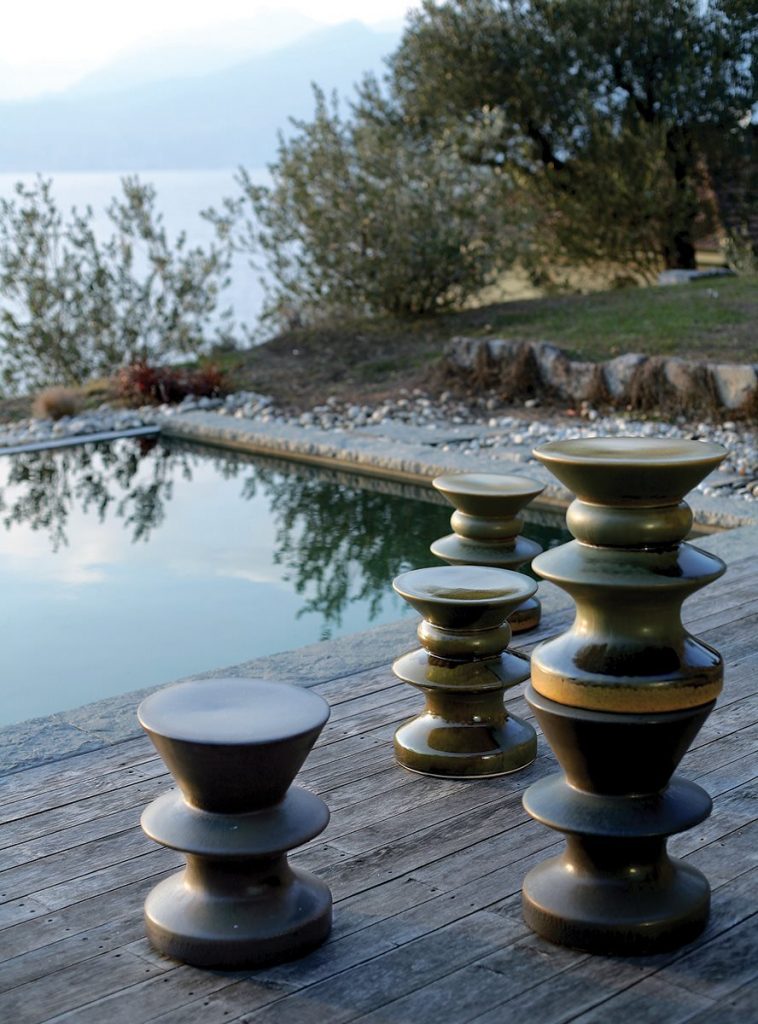 Five Teti side table with a round brown top and a single central metal support, minimalist design next to a pool.