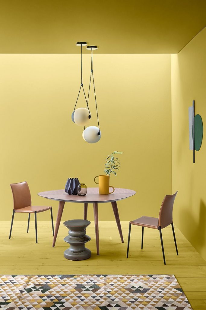 Teti side table with a round black top and a single central metal support, minimalist design on a yellow background.