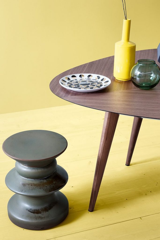 Teti side table with a round black top and a single central metal support, minimalist design on a yellow background.