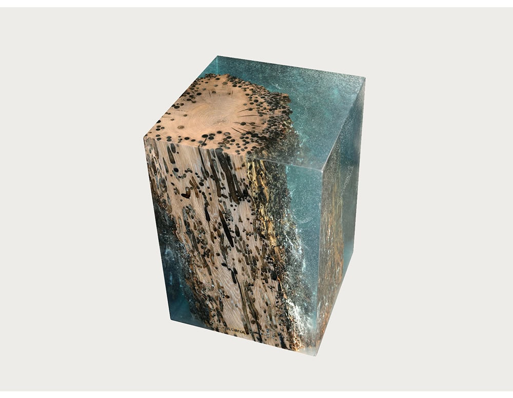 A sculptural stool combining natural wood with clear resin, preserving raw textures in a modern cubic form. Its blend of organic detail and geometric clarity makes it a striking accent piece.
