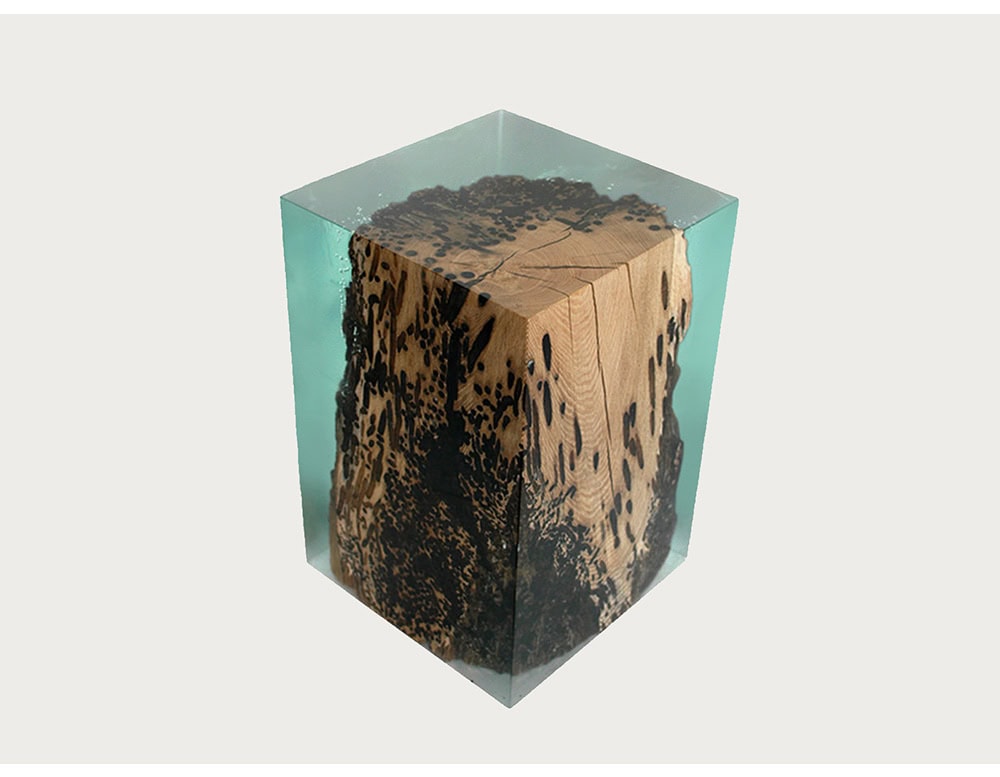 A cube stool featuring raw wood suspended in resin, capturing organic beauty in a modern structure. The contrast of rugged timber and smooth resin offers elegance and durability.